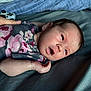 Avery is registered to the contest to win money with this photo: newborn, baby, infant, floral_outfit, bed, hand, controller, gaming, person, skin, face, expression, curious, lying_down, indoor, soft_light, blanket, comfort, young, portrait