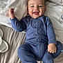 Nathan is registered to the contest to win money with this photo: baby, child, smiling, blue_onesie, bed, pillow, blanket, infant, happy, cute, lying_down, hand, foot, indoor, person, sleepwear, cozy, skin, face, tongue_out