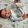 baby, infant, onesie, teddy_bear, blue_clothing, blanket, golf_theme, toy, hand, face, eyes, lying_down, cute, child, indoor, soft_toys, patterned_blanket, smiling, young, playful
