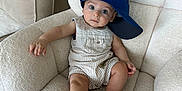 Nathan is registered to the contest to win money with this photo: baby, child, armchair, blue_cap, striped_clothing, indoor, furniture, cute, relaxed, wide_eyes, curious, infant, comfortable, seated, plush, portrait, one_person, soft_texture, casual, hat