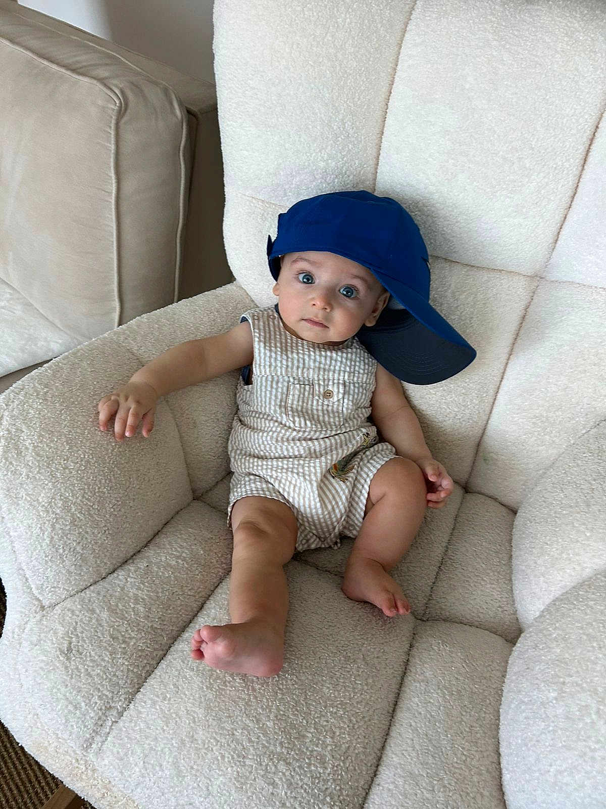 Nathan is registered to the contest to win money with this photo: baby, child, armchair, blue_cap, striped_clothing, indoor, furniture, cute, relaxed, wide_eyes, curious, infant, comfortable, seated, plush, portrait, one_person, soft_texture, casual, hat