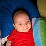 baby, infant, red_clothing, pillow, blanket, soft_texture, smile, face, head, comfort, resting, cute, child, indoor, cozy, colorful, lying_down, young, person, portrait