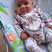 Raya is registered to the contest to win money with this photo: baby, infant, onesie, floral_pattern, baby_seat, smiling, cute, child, face, hand, legs, comfort, indoor, clothing, seat, playful, expression, pattern, colorful, resting