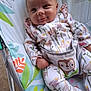 baby, infant, onesie, floral_pattern, baby_seat, smiling, cute, child, face, hand, legs, comfort, indoor, clothing, seat, playful, expression, pattern, colorful, resting