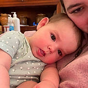 Maisy joined the competition — help win amazing prizes! baby, adult, child, face, hand, onesie, floral_pattern, skin, indoor, cabinet, wooden_furniture, bottle, cosy, affection, family, portrait, closeup, resting, pink_clothing, love