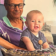 Jean participe au concours pour gagner de l'argent avec cette photo : adult, baby, child, couch, cross_pendant, decor, family, glasses, happy, home, indoor, man, patterned_clothing, person, pillow, portrait, seated, shirt, smile, sofa
