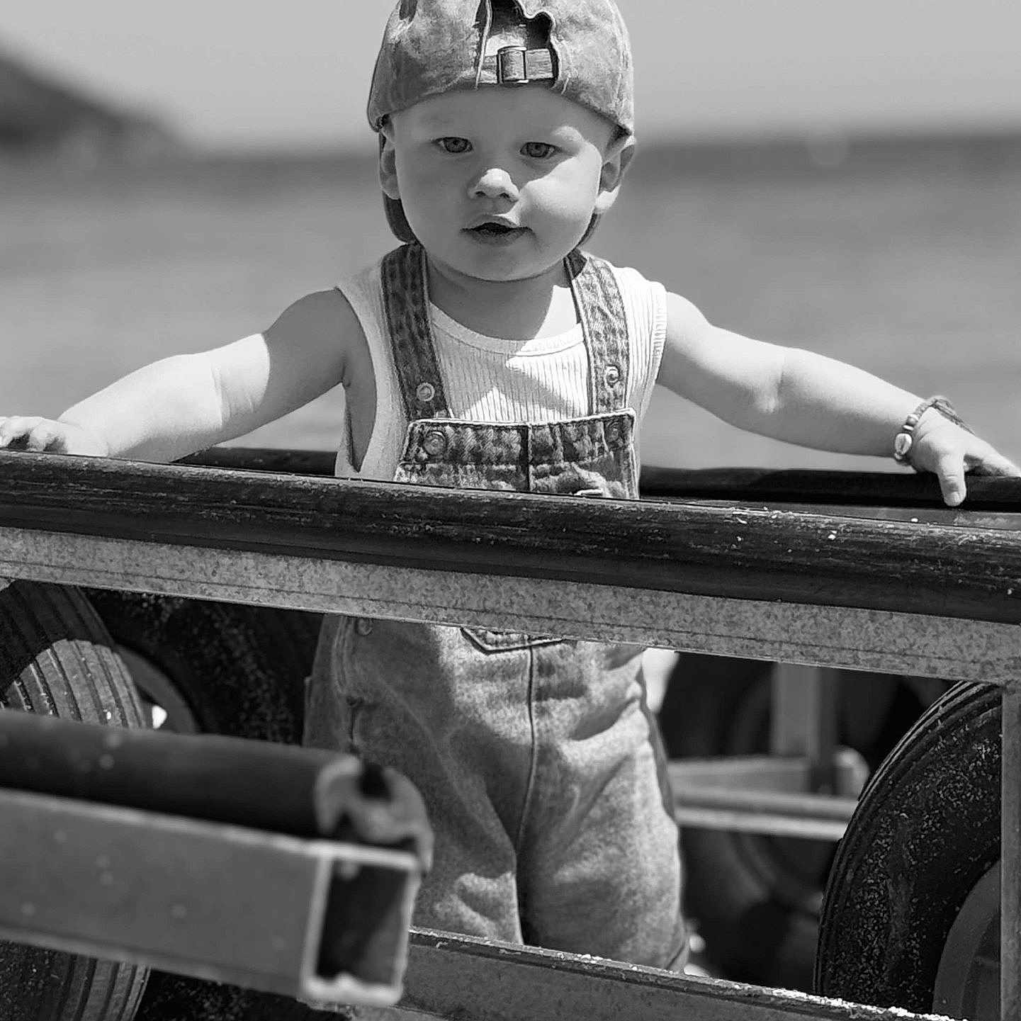 Austin participe au concours pour gagner de l'argent avec cette photo : toddler, child, baby, denim_overalls, cap, barefoot, metal_frame, beach, sea, outdoor, black_and_white, portrait, summer, sunlight, sand, cute, innocence, standing, young_child, casual_clothing