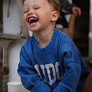 Austin participe au concours pour gagner de l'argent avec cette photo : toddler, child, laughing, blue_sweatshirt, happy, hair, face, smile, outdoor, porch, wood, cup, clothing, person, joy, casual, young_child, emotion, expression, cute