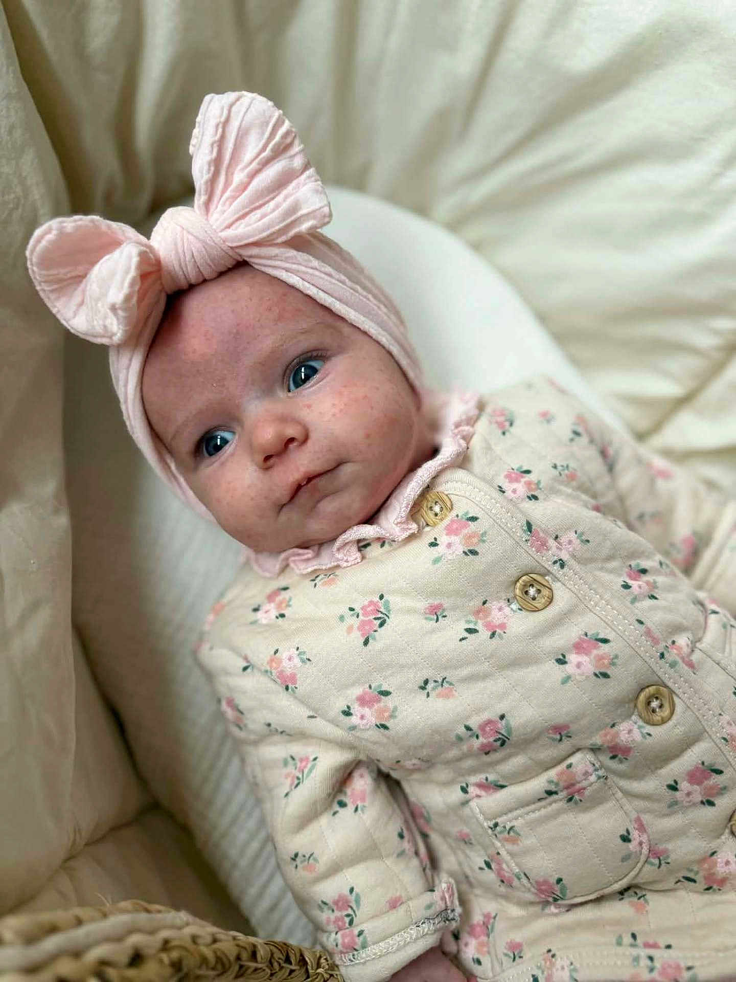Céleste participe au concours pour gagner de l'argent avec cette photo : baby, infant, headband, bow, pink, floral, onesie, clothing, blue_eyes, face, skin, bed, blanket, soft, cute, child, newborn, portrait, indoor, cozy