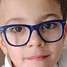 casual, child, childhood, close_up, curly_hair, cute, expression, eyebrows, eyewear, face, friendly, glasses, headshot, indoors, person, portrait, skin, smile, white_shirt, young