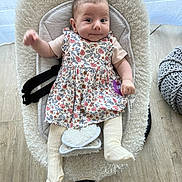 Léonie a rejoint le concours — aidez-le/la à gagner de superbes lots ! baby, infant, child, floral_dress, tights, pacifier, baby_seat, plush, knitted_pouf, wooden_floor, indoor, smiling, face, cute, person, seated, comfortable, home, cozy, expression