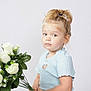 toddler, child, girl, flower_bouquet, white_roses, light_blue_dress, heart_cutout, short_sleeves, blonde_hair, pony_tail, indoor, studio, portrait, holding_flowers, green_leaves, curious_expression, white_background, young_child, cute, casual_clothing