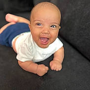Khai is registered to the contest to win money with this photo: baby, infant, smiling, happy, couch, white_shirt, blue_pants, skin, face, hands, eyes, mouth_open, lying_down, indoor, cute, child, young, expression, portrait, human