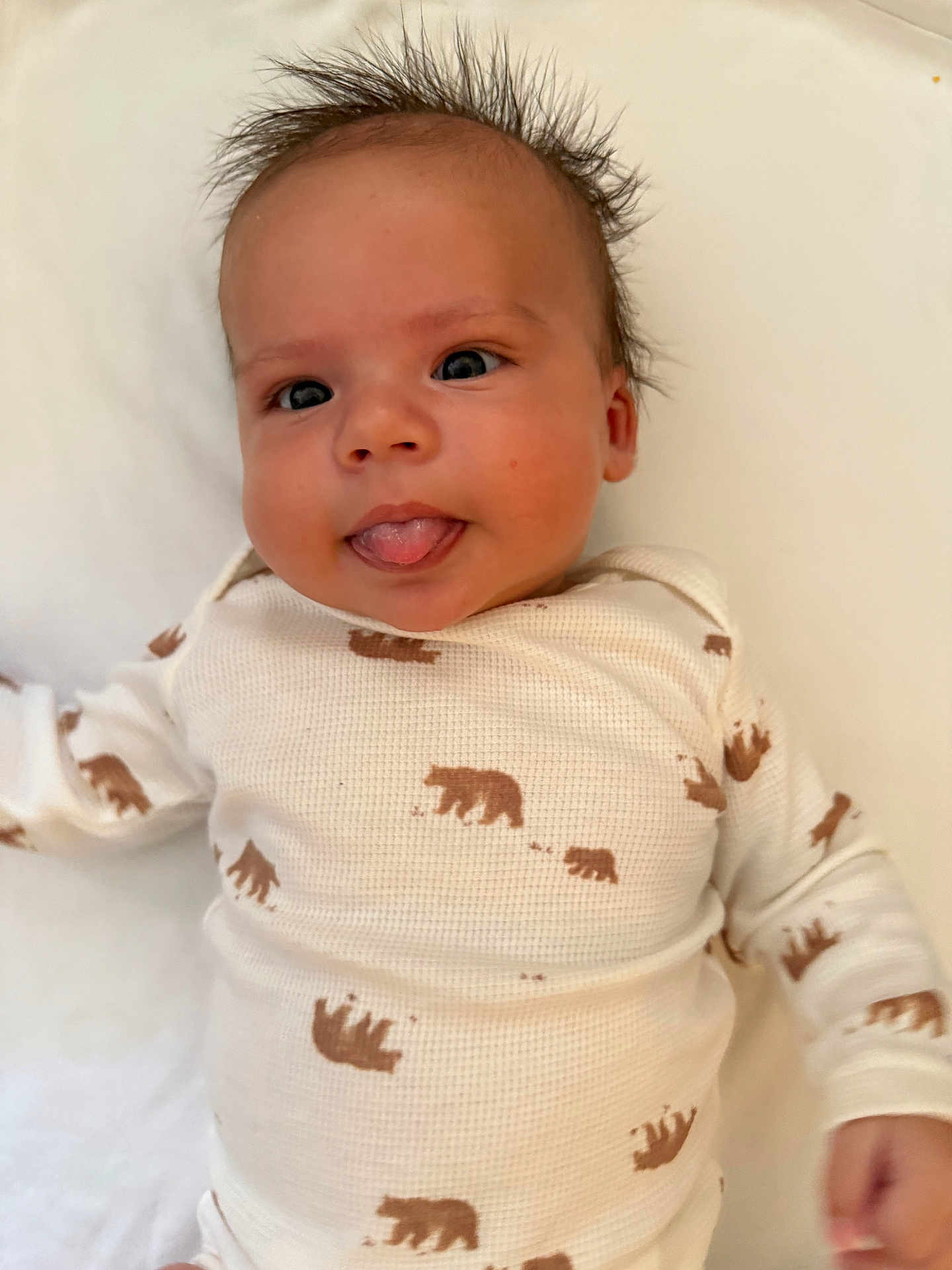 Ibrahim joined the competition — help win amazing prizes! baby, infant, face, tongue, hair, onesie, bear_print, clothing, cute, playful, lying_down, skin, child, expression, smiling, white_background, person, young, funny_face, portrait