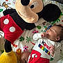 baby, sleeping, plush_toy, mickey_mouse, onesie, colorful, blanket, animal_print, child, cute, soft_toy, indoor, infant, peaceful, resting, toddler, toy, person, bedroom, cozy