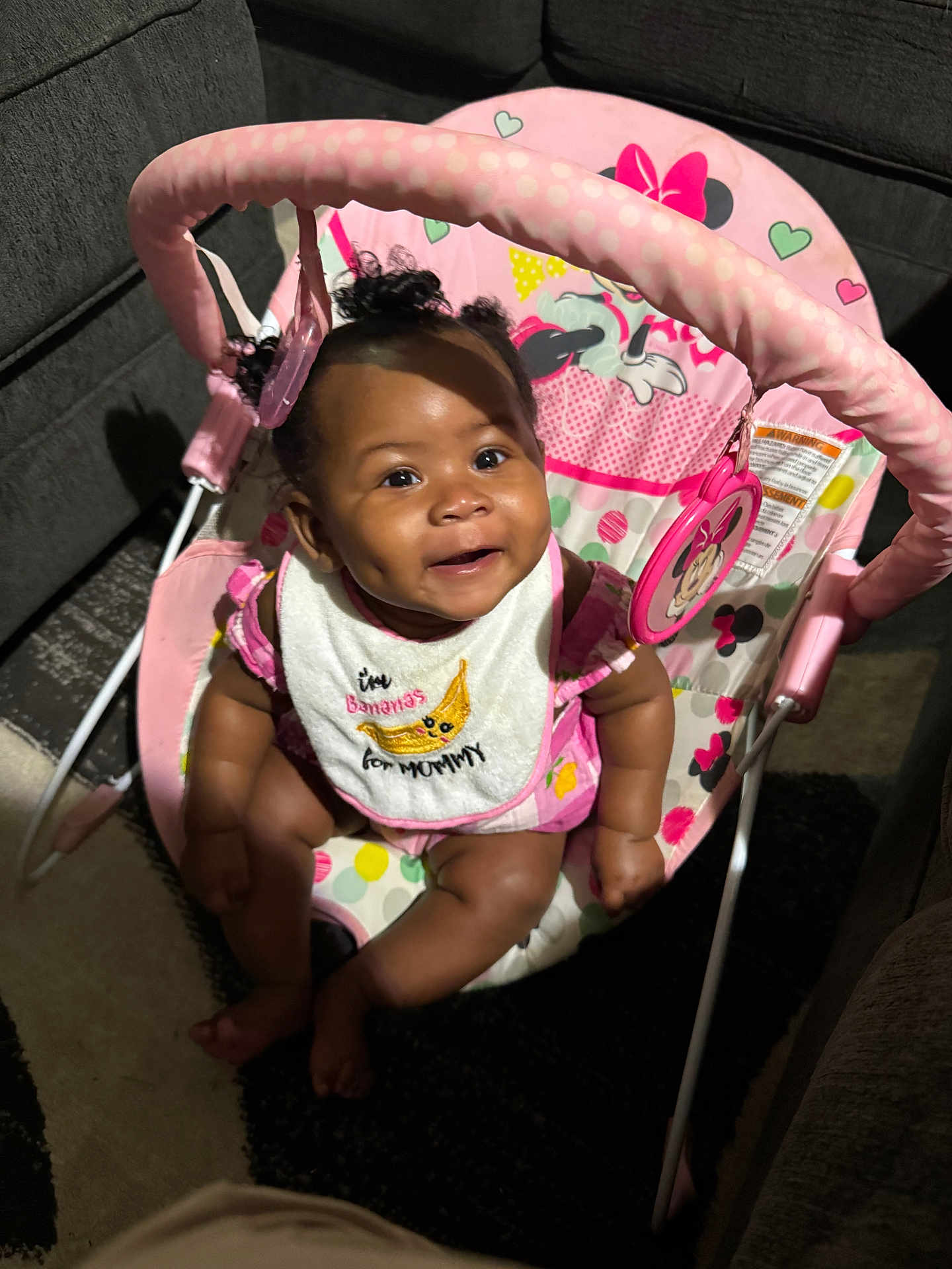Chrissyah is registered to the contest to win money with this photo: baby, infant, smile, dimple, curly_hair, pink, bib, baby_rocker, minnie_mouse, toy, happy, cute, indoor, carpet, furniture, child, seat, clothing, person, cheerful