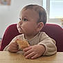 baby, infant, child, highchair, red_chair, bread, food, table, hands, cheeks, side_profile, portrait, indoor, natural_light, curious, soft_focus, cozy, cute, sitting, expression