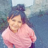 casual_clothing, child, cute, daylight, earrings, flower, girl, hair_tied, handbag, happy, outdoor, pavement, pink_jacket, portrait, smiling, standing, stone_wall, urban, white_sneakers, young