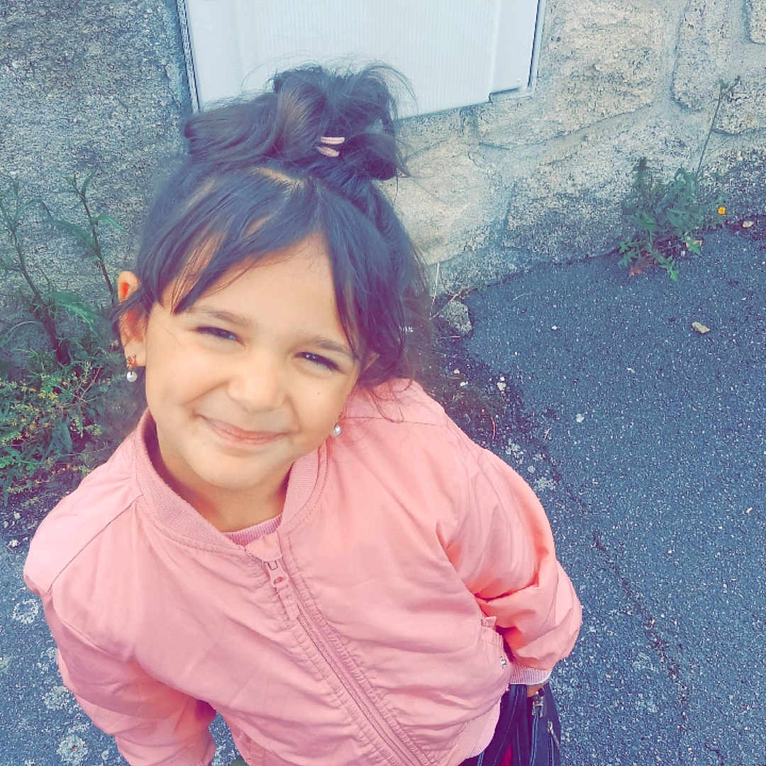 Jena participe au concours pour gagner de l'argent avec cette photo : child, girl, smiling, pink_jacket, white_sneakers, flower, handbag, pavement, stone_wall, outdoor, casual_clothing, happy, standing, young, hair_tied, earrings, urban, daylight, portrait, cute