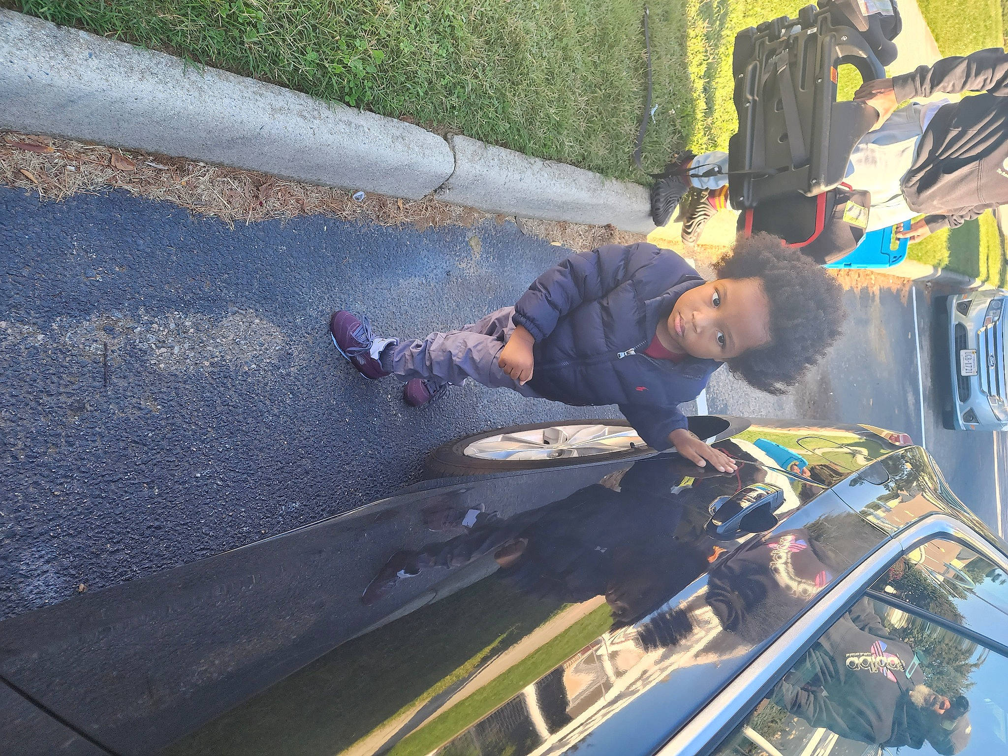 Jerry Jr is registered to the contest to win money with this photo: asphalt, auto_part, automotive_exterior, automotive_tire, automotive_wheel_system, automotive_window_part, bumper, car, electric_blue, glass, hood, leisure, motor_vehicle, person, recreation, road_surface, t_shirt, toddler, vehicle, vehicle_door