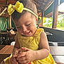 baby, bottle, bow, casual, chair, child, curious, cute, happy, headband, holding, indoor, infant, natural_light, person, portrait, smiling, table, wooden_structure, yellow_dress