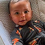 baby, infant, child, face, eyes, hand, onesie, clothing, pattern, cushion, indoor, portrait, cute, smiling, babywear, seat, comfort, expression, reaching, skin