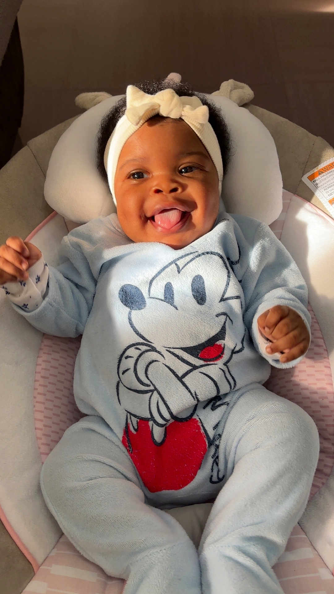Elhyana participe au concours pour gagner de l'argent avec cette photo : baby, child, infant, headband, mickey_mouse, onesie, blue_clothing, smile, tongue_out, cushion, baby_seat, indoor, happy, cute, person, soft_fabric, closeup, playful, cozy, sunlight