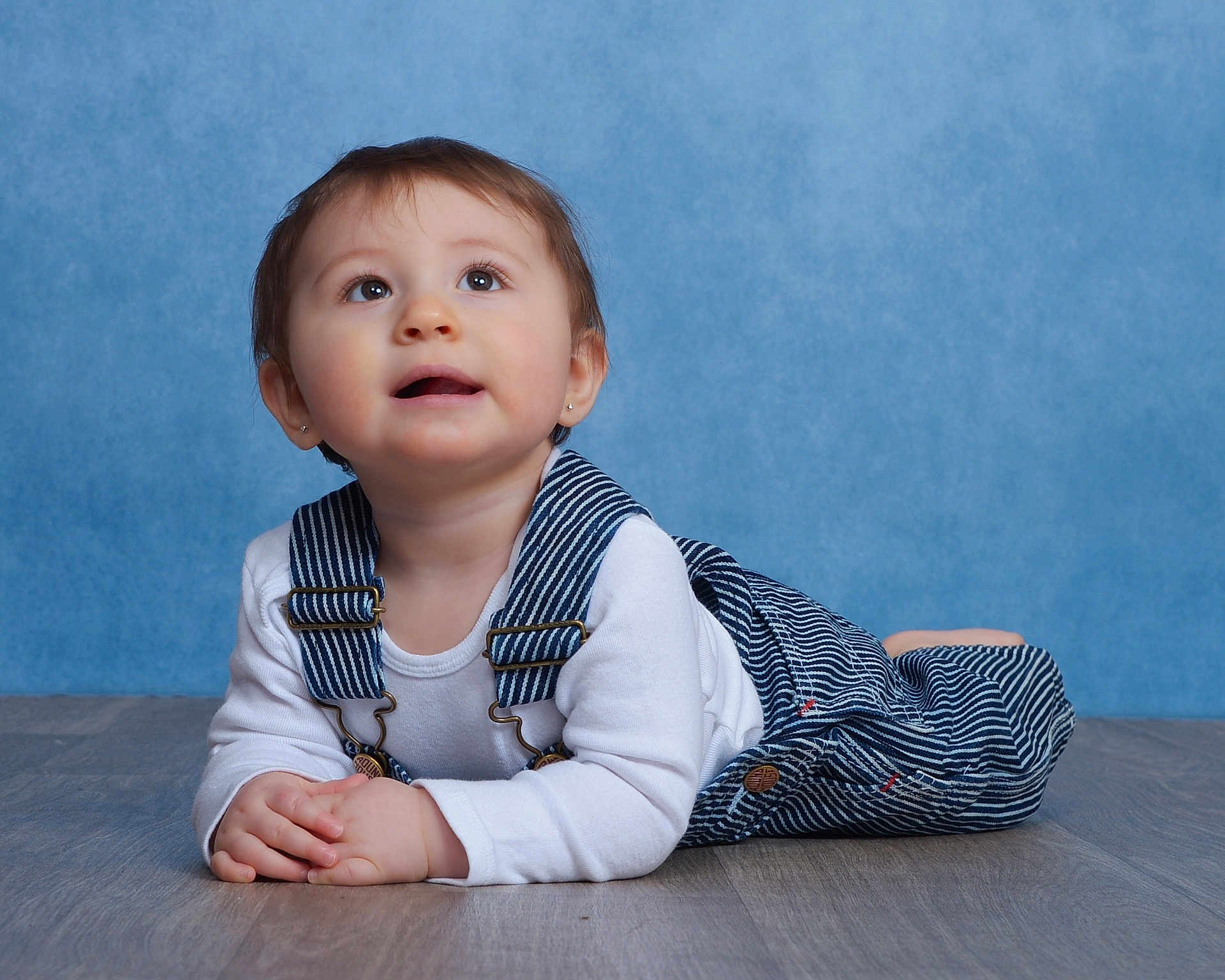 Emi joined the competition — help win amazing prizes! baby, child, infant, portrait, overalls, white_shirt, floor, blue_background, curious, cute, lying_down, hands_clasped, studio_photo, young_child, face, eyes, hair, indoor, clothing, expression