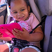 Nevaeh is registered to the contest to win money with this photo: toddler, child, car_seat, birthday_badge, tablet, smiling, hair_beads, summer_clothes, casual_wear, sunlight, car_interior, seatbelt, happy, cute, portrait, close_up, baby_girl, playful, technology, fun