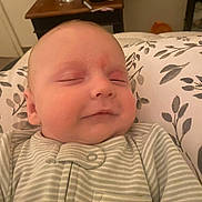 Hudson joined the competition — help win amazing prizes! baby, sleeping, onesie, striped_clothing, infant, face, peaceful, smile, pillow, floral_pattern, indoor, table, water_bottle, wooden_furniture, room, head, close_up, person, resting, soft_lighting