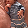 baby, sleeping, pajamas, curly_hair, cushion, pink, blue, striped_clothing, infant, hand, face, soft_fabric, cozy, resting, indoors, cute, peaceful, child, person, adorable