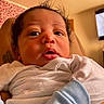 Daylin is registered to the contest to win money with this photo: baby, infant, face, eyes, mouth, clothing, white_outfit, blue_sleeves, curly_hair, indoor, television, furniture, skin, person, newborn, portrait, cute, expression, child, home