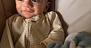 Sebastian joined the competition — help win amazing prizes! baby, infant, child, smile, face, eyes, hand, blanket, striped_clothing, onesie, cushion, soft_toy, cozy, indoors, portrait, cute, warm_lighting, relaxed, comfort, young