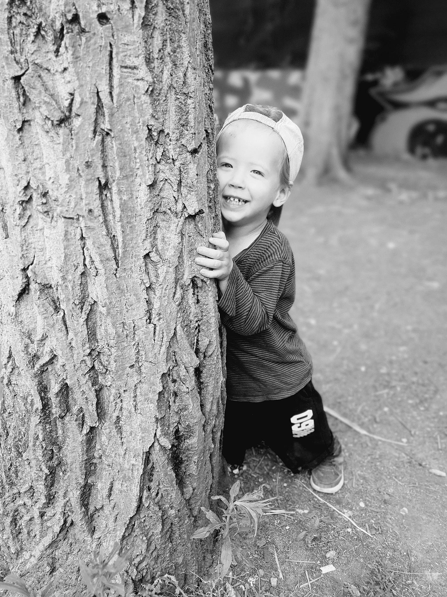Johan a rejoint le concours — aidez-le/la à gagner de superbes lots ! black_and_white, child, eye, fun, hide_and_seek, joy, monochrome, monochrome_photography, people, person, photograph, photography, plant, play, skin, smile, snapshot, standing, toddler, tree