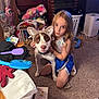 child, dog, indoor, carpet, toy, laundry_basket, brush, glove, headband, ears, furniture, brick_wall, door, hair_brush, clothing, pet, floor, young_girl, curly_hair, playful