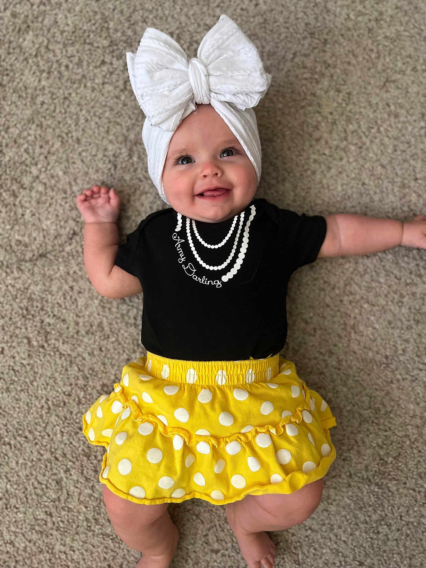 Harper is registered to the contest to win money with this photo: baby, child, smiling, headwrap, bow, black_shirt, yellow_skirt, polka_dots, carpet, infant, cute, happy, lying_down, apparel, portrait, indoors, person, chubby_cheeks, hand, feet