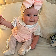 Dream is registered to the contest to win money with this photo: baby, child, smile, pink_bow, headband, tights, dress, bed, pillow, cute, indoors, person, sitting, infant, hand_holding, soft_lighting, happy, face, white_clothing, playful