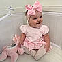 baby, child, pink_bow, headband, dress, crib, stuffed_animal, bunny, toy, smiling, sitting, toddler, indoor, cute, happy, soft_toy, person, infant, pale_pink, baby_clothes