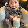 toddler, child, baby, face, eyes, onesie, heart_pattern, curly_hair, foot, toes, sippy_cup, chair, cloud_pattern, star_pattern, indoor, portrait, seated, expression, casual_clothing, soft_lighting