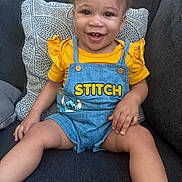 Cym Phonie is registered to the contest to win money with this photo: toddler, child, smiling, sitting, yellow_shirt, denim_overalls, stitch_character, couch, pillow, happy, cute, indoor, portrait, face, person, clothing, shorts, baby, young_child, home