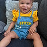 toddler, child, smiling, sitting, yellow_shirt, denim_overalls, stitch_character, couch, pillow, happy, cute, indoor, portrait, face, person, clothing, shorts, baby, young_child, home