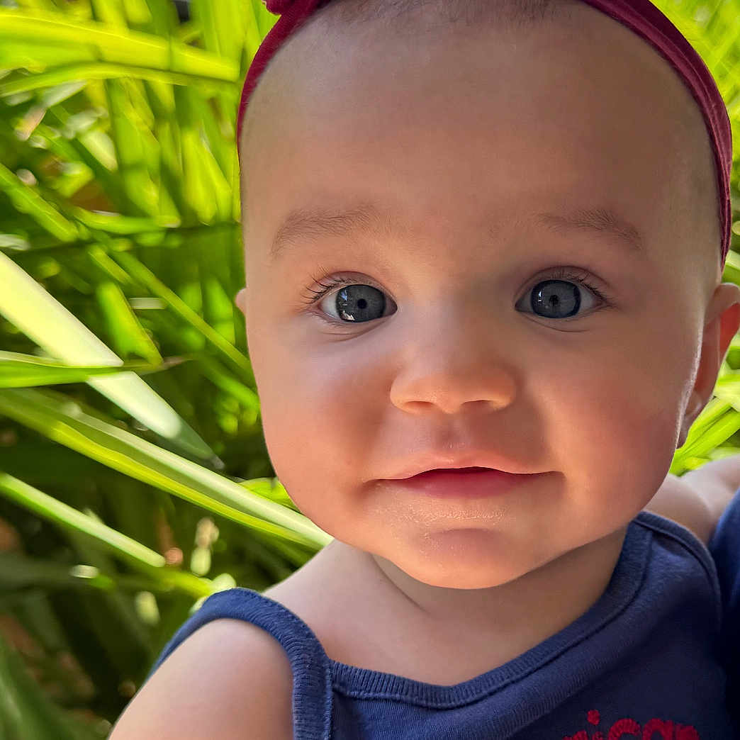 Malia joined the competition — help win amazing prizes! baby, child, headband, outdoor, greenery, plants, smile, face, tank_top, blue_clothing, cute, portrait, young_child, skin, eyes, closeup, sunlight, nature, happy, person