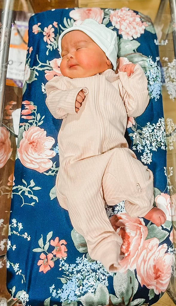 Tatum is registered to the contest to win money with this photo: azure, baby, baby_products, baby_sleeping, baby_toddler_clothing, blue, child, electric_blue, floral_design, headwear, linens, pattern, peach, person, petal, pink, sitting, sleeve, textile, toddler