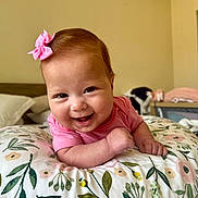 Salomé is registered to the contest to win money with this photo: baby, child, closeup, cute, expression, face, floral_cushion, happy, head, indoors, infant, lying_down, person, pink_bow, pink_shirt, portrait, room, skin, smiling, young