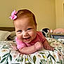 Salomé is registered to the contest to win money with this photo: baby, infant, smiling, pink_bow, pink_shirt, pillow, floral_pattern, indoors, happy, cute, child, face, head, skin, person, resting, lying_down, closeup, cheerful, young