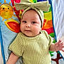 baby, child, infant, headband, bow, green_clothing, ribbed_fabric, play_mat, colorful, sun, smiling_face, cute, portrait, lying_down, hand, skin, indoors, bright, happy, young