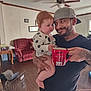 Century joined the competition — help win amazing prizes! baby, child, man, tattoos, mug, red_mug, polka_dot_clothing, living_room, christmas_tree, sofa, wood_floor, ceiling_fan, table, mirror, window, indoor, holding, smiling, person, family_moment
