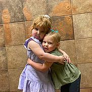 Century is registered to the contest to win money with this photo: children, hug, tiled_wall, dress, green_top, pants, indoor, cute, young_girls, affection, friendship, smile, blonde, redhead, child, portrait, casual_clothing, together, happy, playful