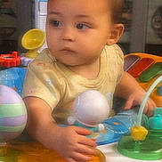 Joanna joined the competition — help win amazing prizes! baby, child, infant, toys, activity_center, colorful, indoor, cute, play, hand, face, young, person, seat, expression, curious, soft_lighting, clothing, background, toddler