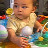 baby, child, infant, toys, activity_center, colorful, indoor, cute, play, hand, face, young, person, seat, expression, curious, soft_lighting, clothing, background, toddler